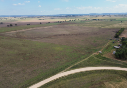 Aerial shot of Dunedoo Energy Project site in NSW: open green field, gravel road, site team and vehicles, clear blue sky.