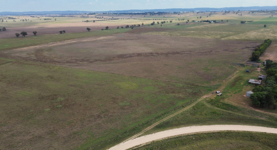 Aerial shot of Dunedoo Energy Project site in NSW: open green field, gravel road, site team and vehicles, clear blue sky.